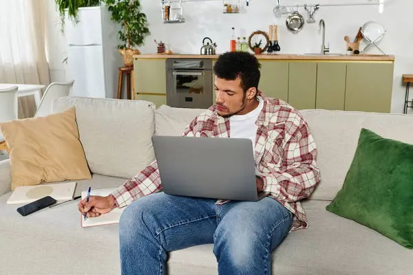 Man engaged in work on a laptop while seated comfortably on a sofa at home. — Stock Photo