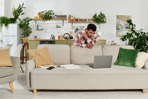 Handsome young man focused on his laptop, surrounded by greenery and a stylish interior. — Stock Photo