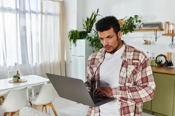 Beau jeune homme se concentre sur ordinateur portable dans un intérieur élégant rempli de verdure. — Photo de stock