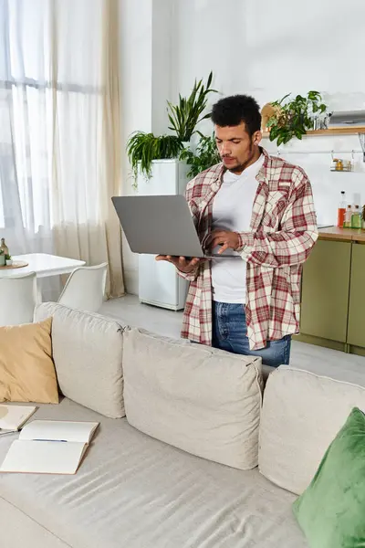 Handsome young man types on a laptop while standing in a stylish living room — Stock Photo