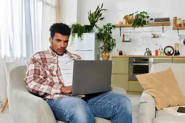 A young handsome man is focused on his laptop while sitting in a modern living room. — Stock Photo