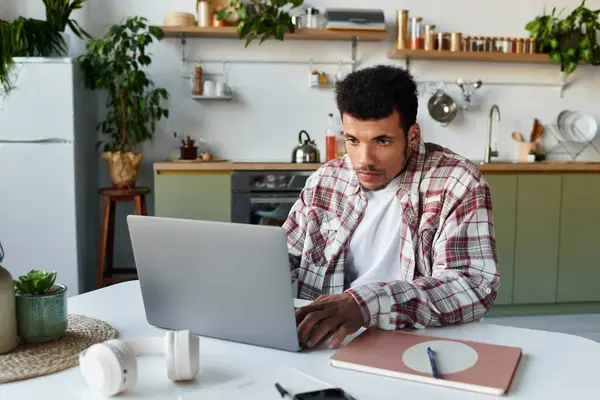 Focused young man engages with his laptop at a bright table surrounded by greenery. — Stock Photo