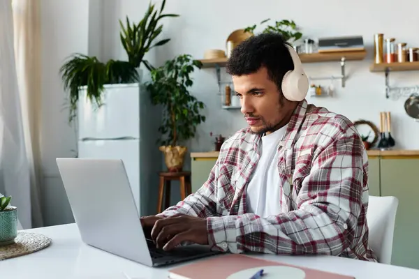 Handsome young man wearing headphones focuses intently on his laptop in cozy office. — Stock Photo
