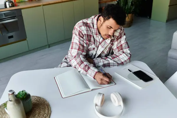 Handsome young man is focused on writing notes in a notebook at a stylish kitchen table. — Stock Photo