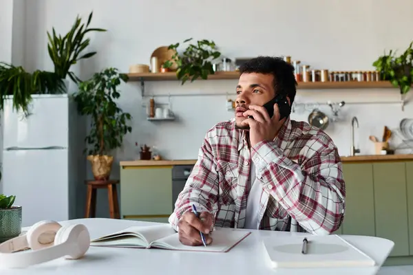 Mann konzentriert sich auf ein Telefonat, während er Notizen in einem gemütlichen Home Office voller Pflanzen schreibt. — Stockfoto