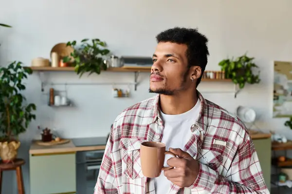 Man stands thoughtfully holding a coffee mug in a stylish kitchen filled with plants. — Stock Photo