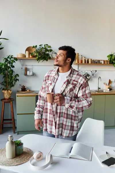 Un giovane uomo si trova in una cucina luminosa, sorseggiando un drink caldo e osservando i dintorni. — Foto stock