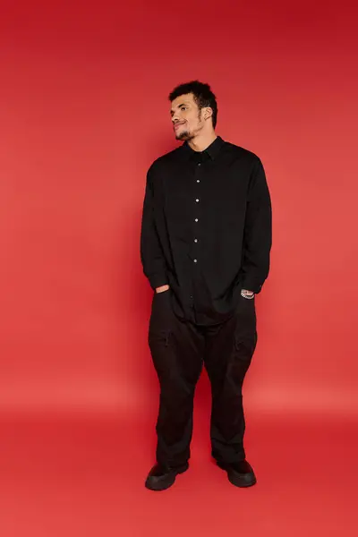 A young handsome man stands confidently, wearing black attire, with a striking red backdrop. — Stock Photo