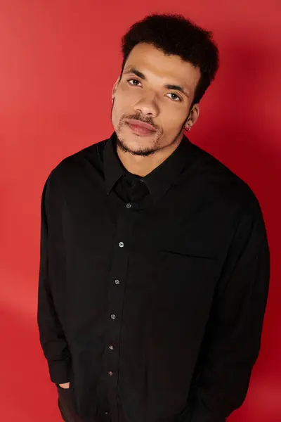 Un hombre joven y guapo con una elegante camisa negra se levanta relajado contra el vibrante rojo. - foto de stock
