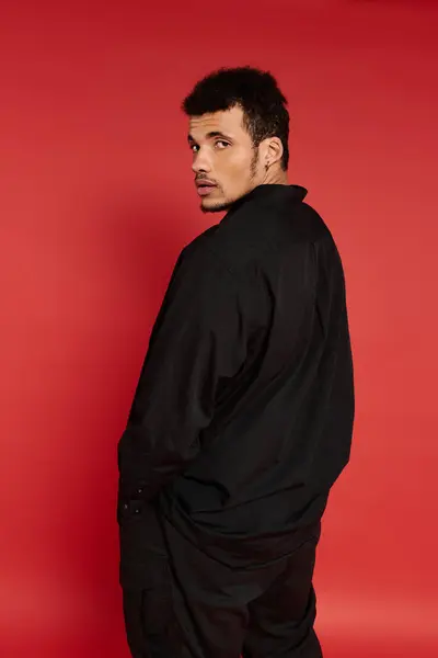Der junge Mann mit dem stylischen Look steht selbstbewusst vor knallrotem Hintergrund. — Stockfoto
