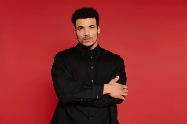 A young handsome man stands with crossed arms, showcasing a smart and trendy black shirt. — Stock Photo
