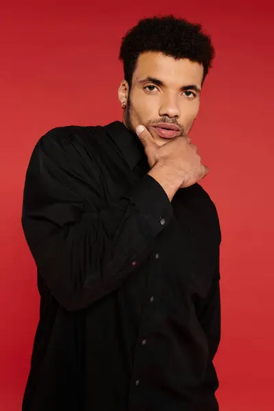 En un llamativo escenario rojo, un joven guapo muestra su pose confiada en una camisa negra. - foto de stock