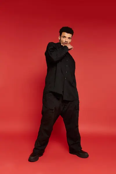 Stylish young man stands confidently in casual black clothing with a striking red background. — Stock Photo