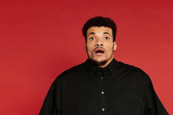 A young man with a surprised expression stands indoors against a bold red background. — Stock Photo