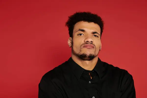 A young man poses confidently with a strong expression in front of a bright red wall. — Stock Photo