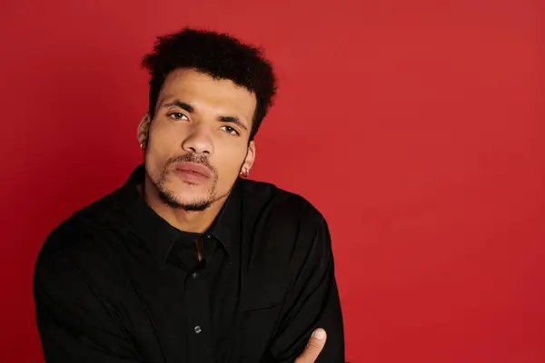 Handsome young man gazes thoughtfully while dressed in a black shirt on a red backdrop — Stock Photo