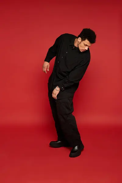 Stylish young man dressed in black striking a casual pose in a vivid red setting. — Stock Photo