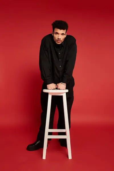 A young handsome man stands on a stool, leaning forward with a striking expression. — Stock Photo