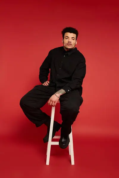 A young handsome man poses confidently on a white stool in front of a bright red background. — Stock Photo