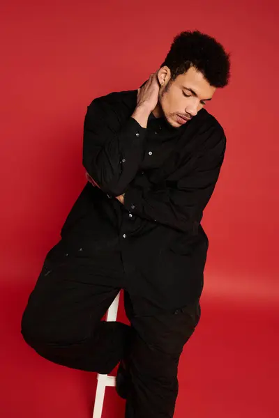 Un joven guapo se sienta pensativamente con la mano en el cuello, vestido de negro. - foto de stock