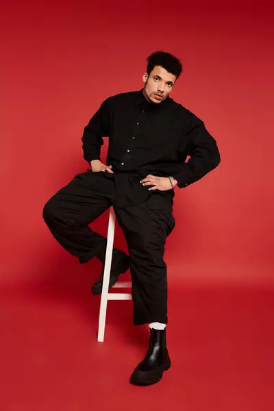 Handsome young man sits on a stool with a striking expression in a bold, simple setting. — Stock Photo