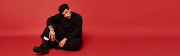 The young man sits comfortably on the floor, wearing stylish clothing and showing confidence. — Stock Photo