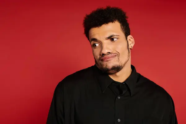 A handsome young man displays a curious expression in front of a bold red backdrop. — Stock Photo