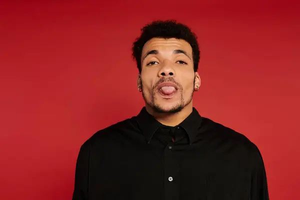 A young handsome man poses with a playful expression, tongue out, against a vibrant red backdrop. — Stock Photo