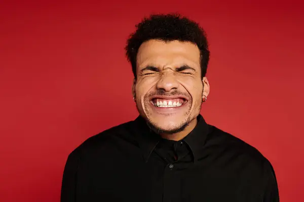 Um homem bonito jovem com uma expressão alegre está com um pano de fundo vermelho, irradiando positividade. — Fotografia de Stock