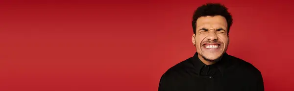 A young handsome man displays a big smile, enjoying a joyful moment with a bright red backdrop. — Stock Photo