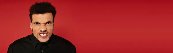 Handsome young man displays a unique facial expression in front of a red backdrop. — Stock Photo