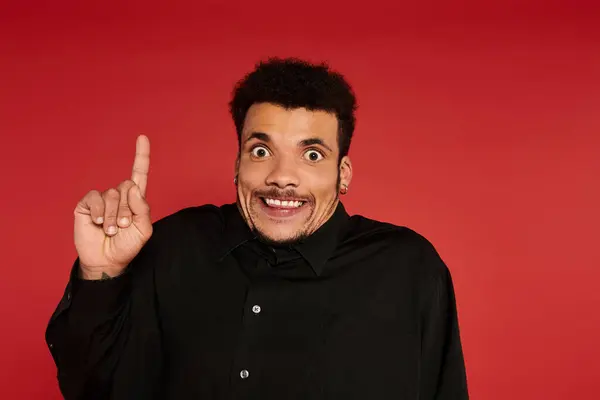 A young handsome man shows excitement with a raised finger in front of a red background. — Stock Photo