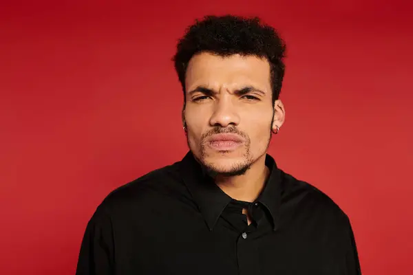 A young man with stylish hair and a serious expression stands against a bright red background. — Stock Photo
