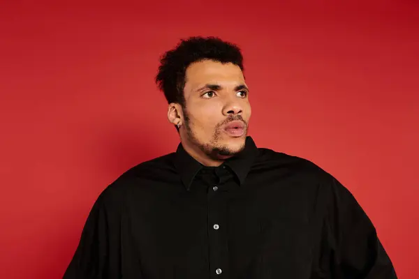 Handsome young man wearing a black shirt looks surprised against a vibrant red backdrop. — Stock Photo