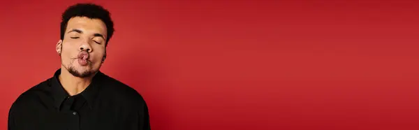 A young handsome man stands against a vibrant red backdrop, playfully posing. — Stock Photo