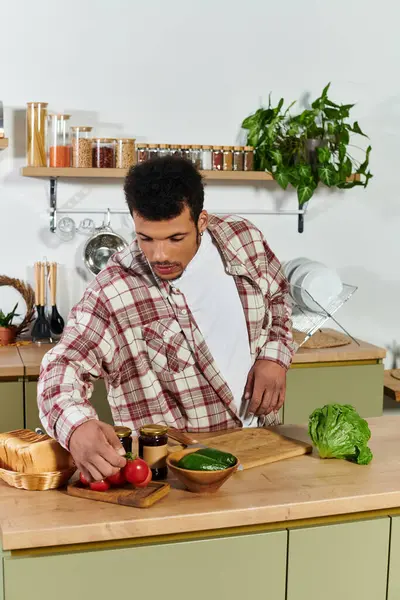 A young handsome man arranges fresh vegetables on a wooden cutting board in a bright kitchen. — Stock Photo