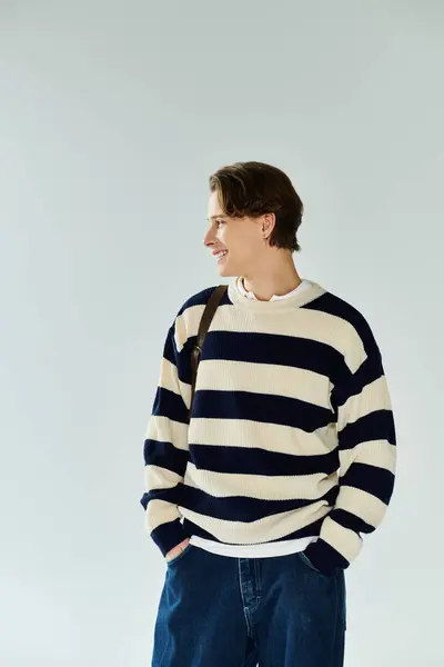 A stylish young student in a striped sweater stands confidently in a studio, embracing college life. — Stock Photo