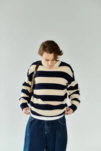 A young man dressed in a striped sweater prepares for his college journey in a studio. — Stock Photo