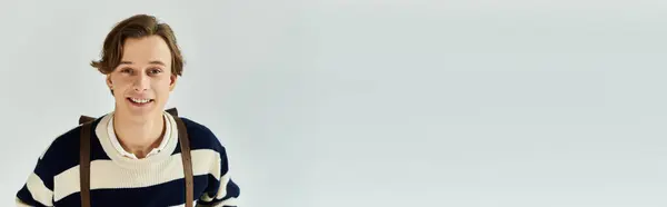 A handsome young man with a warm smile showcases college fashion in a cozy studio setting, banner — Stock Photo