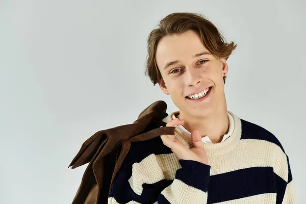 Young student in a striped sweater smiles warmly in a cozy studio, embodying youth culture. — Stock Photo