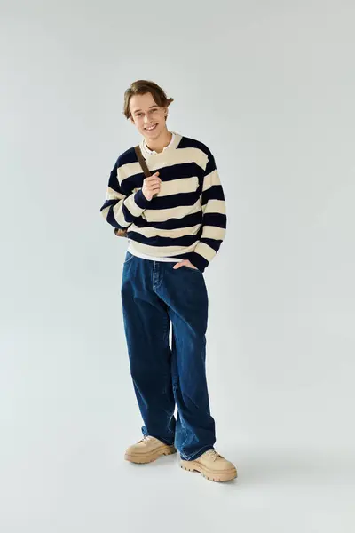 Handsome young man dons a striped sweater, embodying college fashion and youth culture in a studio. — Stock Photo