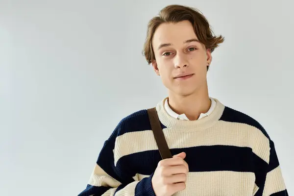 A stylish young man in a striped sweater poses warmly in astudio, exuding confidence. — Stock Photo