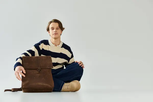 A young man in a striped sweater sits comfortably in a studio, embodying youthful fashion. — Stock Photo