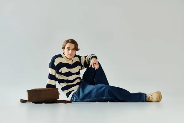 A young man wearing a striped sweater relaxed on the floor in a studio, showcasing modern fashion. — Stock Photo