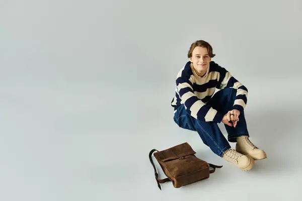 A handsome young man wearing a striped sweater sits on a studio floor, exuding confidence. — Stock Photo