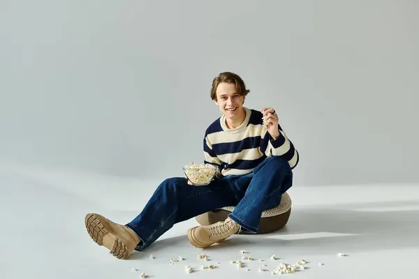 A relaxed young student in a striped sweater shares a joyful moment with popcorn, embodying youth. — Stock Photo