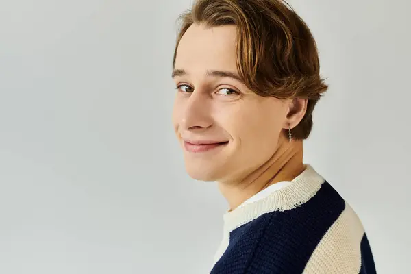 A cheerful young man smiles warmly in a cozy studio environment, showcasing youthful style. — Stock Photo