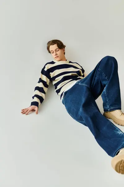 A stylish young man in a striped sweater relaxes in a contemporary studio, exuding college energy. — Stock Photo