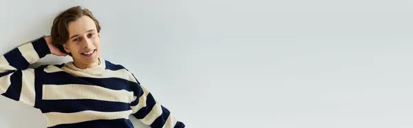 A cheerful young man enjoys a moment in a cozy striped sweater, embodying college spirit, banner — Stock Photo