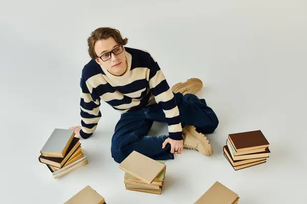 Handsome young man sits on the floor with books around him, reflecting on his college life. — Stock Photo